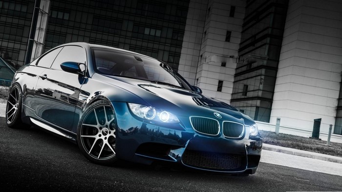 Blue BMW E92 M3 parked in front of modern buildings