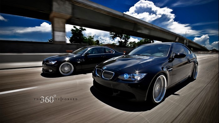 Two black BMWs driving on a highway