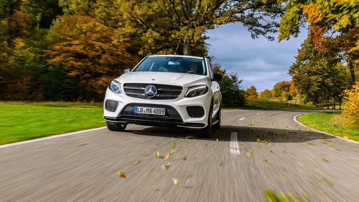 White Mercedes-Benz GLE driving on a road in autumn