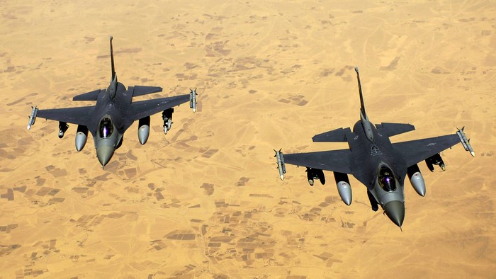Two F-16 fighter jets flying over desert terrain