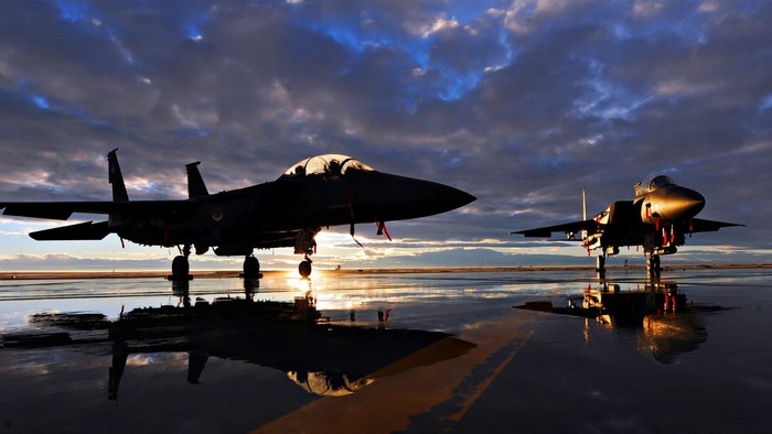Two F-15 fighter jets on a wet tarmac at sunset