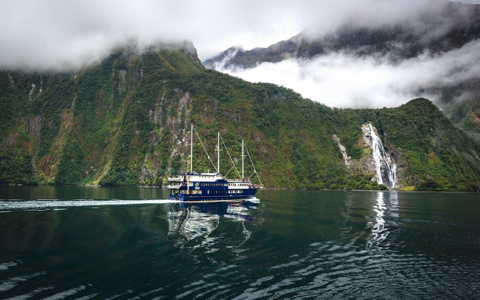 Boat sailing in a fjord with waterfalls and mountains