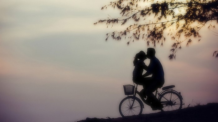 Couple kissing on a bicycle at sunset