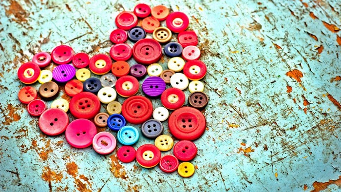Heart shape made of colorful buttons on a distressed wooden surface