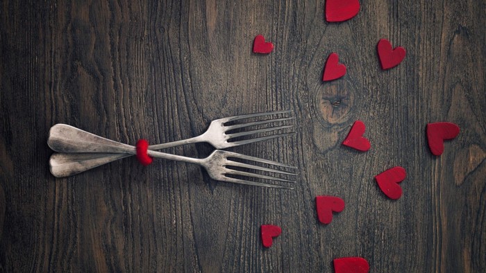 Two forks tied with red ribbon and red hearts on wood