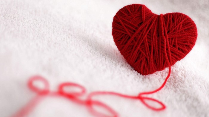 Red yarn heart on white textured surface