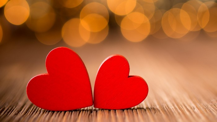 Two red hearts on a wooden surface with bokeh lights