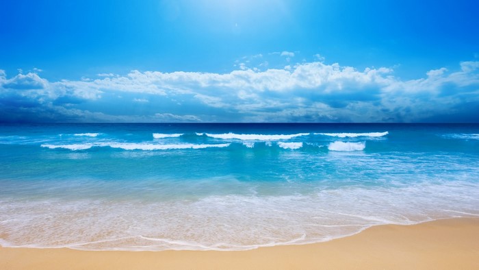 Ocean waves on a sandy beach under a blue sky
