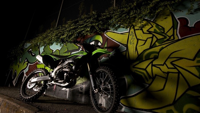 Kawasaki dirt bike parked against graffiti wall