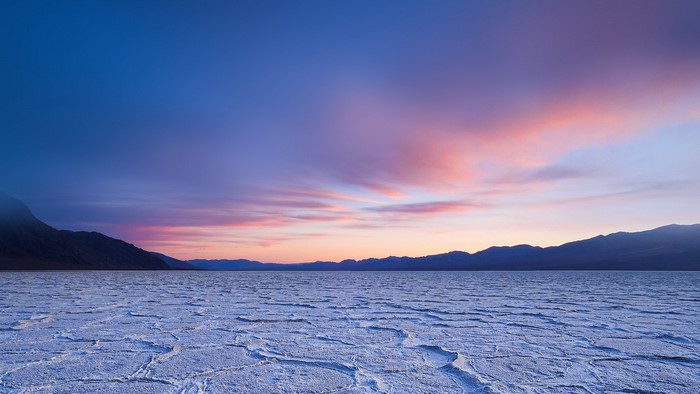 Sunrise over a cracked salt flat with mountains