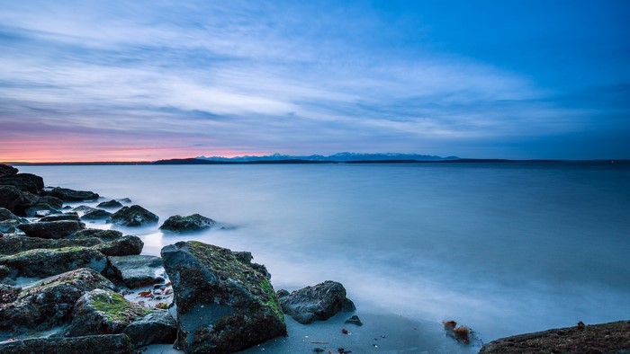 Rocks on a beach with mountains and sunset sky