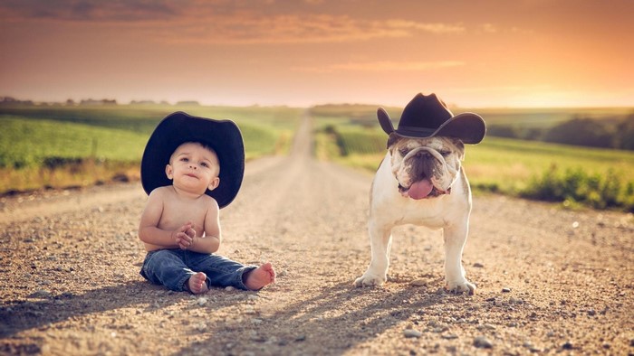 Baby and Bulldog Wearing Cowboy Hats on a Dirt Road