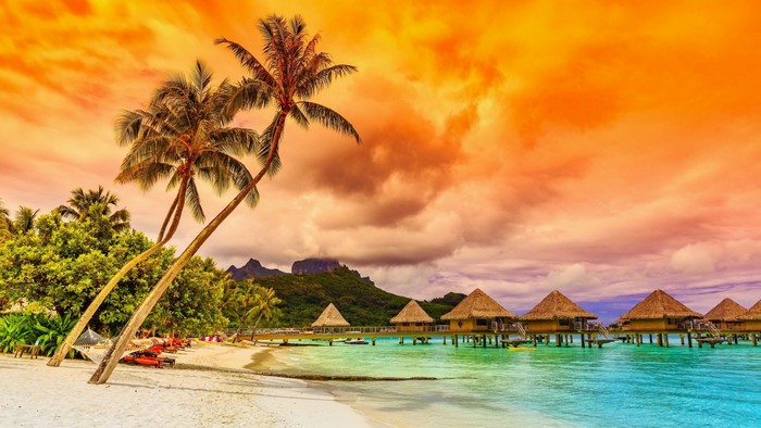Tropical beach with overwater bungalows at sunset