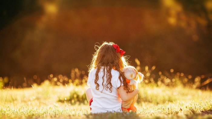Girl with a doll in a field at sunset