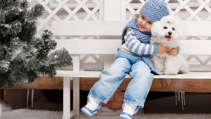 Girl hugging a white dog on a snowy bench