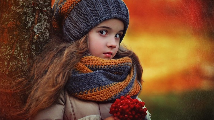 Girl in knitted hat and scarf holding red berries