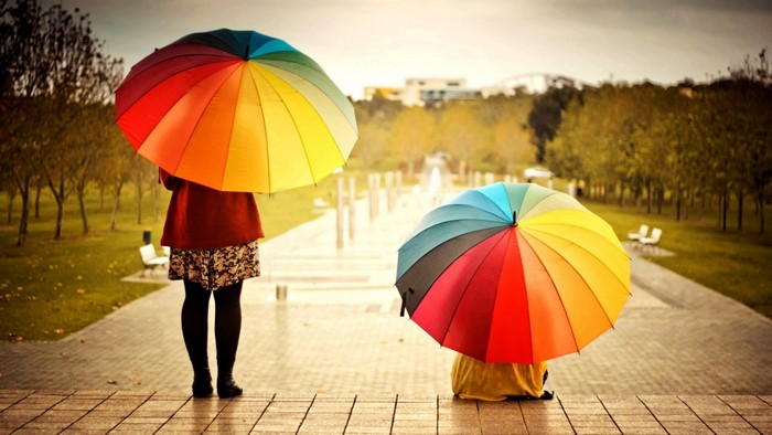 Two people with rainbow umbrellas in a park
