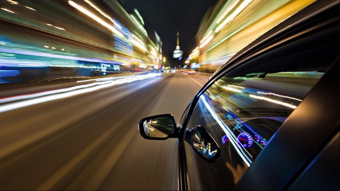 Car driving through city at night with light trails