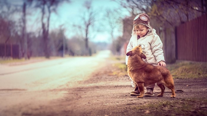 Boy in aviator hat with dog on dirt road