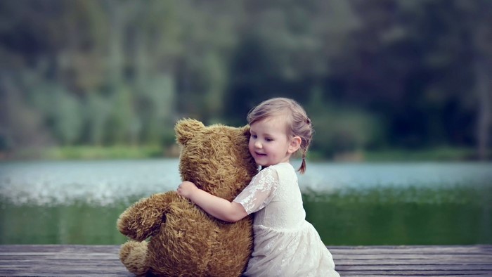 Girl hugging a teddy bear by a lake