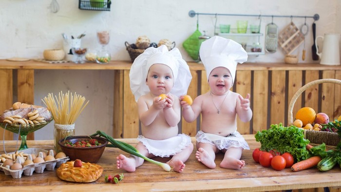 Two babies dressed as chefs in a kitchen