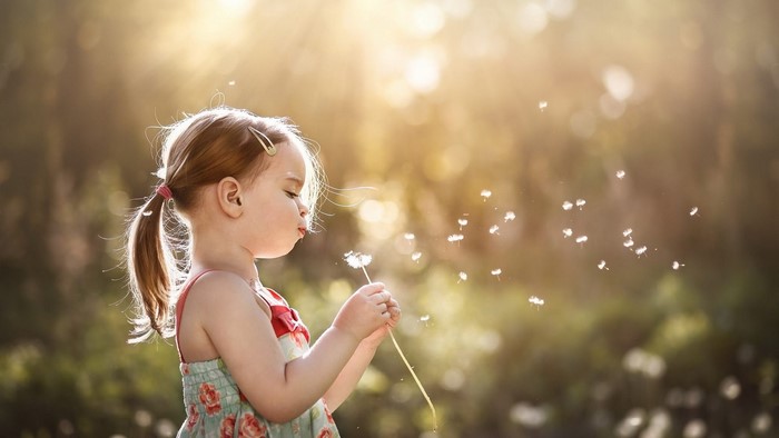 Little Girl Blowing Dandelions in Garden