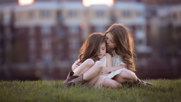 Two young sisters hugging on a grassy hill