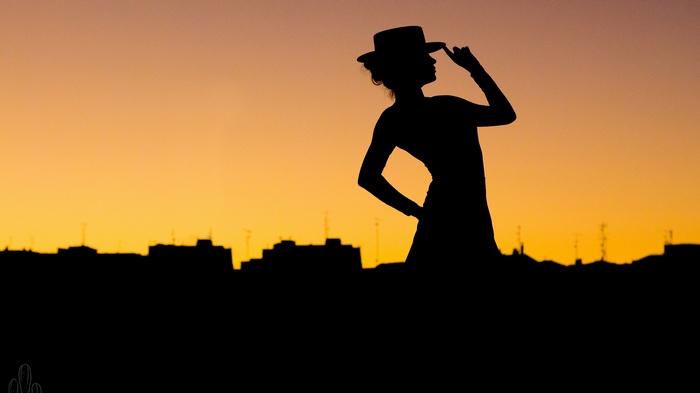 Woman in hat silhouette at dusk over city