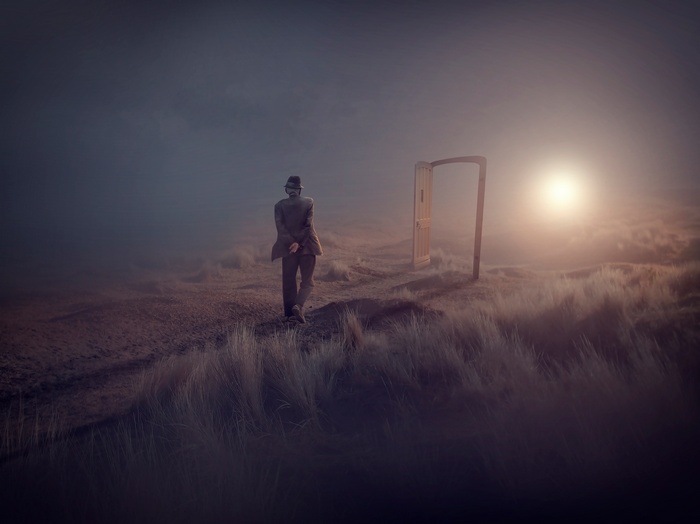 Man in suit walks towards an open door in a foggy landscape
