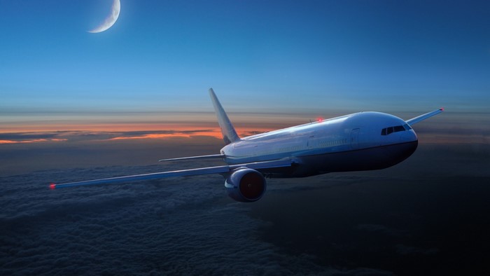 Commercial jet airplane flying over clouds at sunset with moon