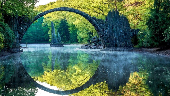 Stone arched bridge over a misty lake with reflections