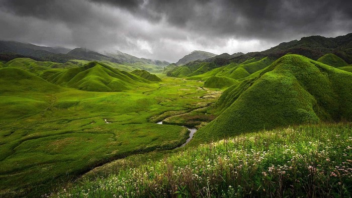 Green rolling hills and mountains under cloudy sky