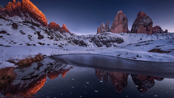 Frozen mountain lake reflecting rocky peaks at sunset