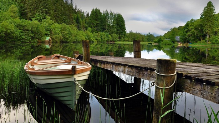 Boat docked at a wooden pier on a calm lake surrounded by trees