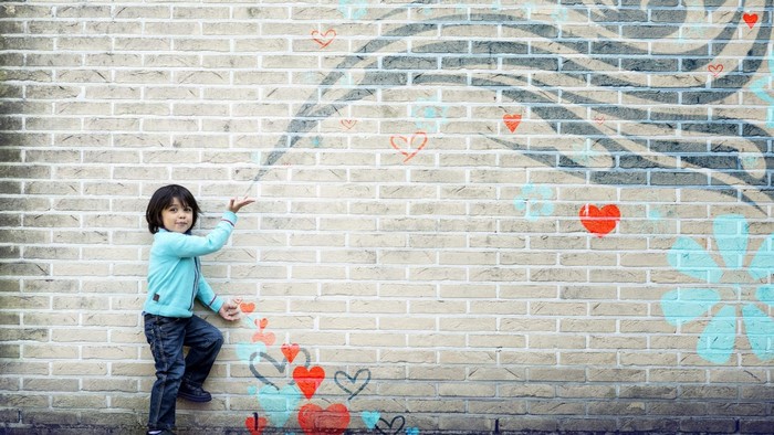 Boy in blue jacket near brick wall with art
