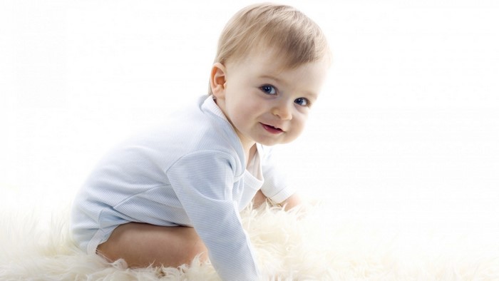Baby boy in blue onesie on white rug