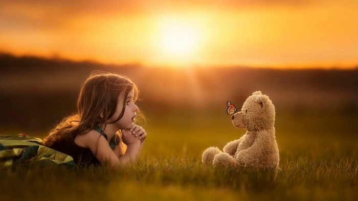 Girl and teddy bear with butterfly at sunset