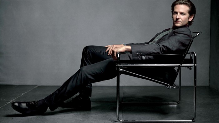 Bradley Cooper in a dark suit sitting in a chair