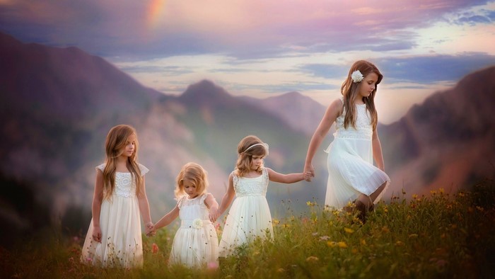 Four young girls in white dresses holding hands in a meadow