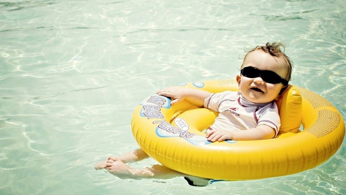 Baby wearing sunglasses in a yellow float in a pool