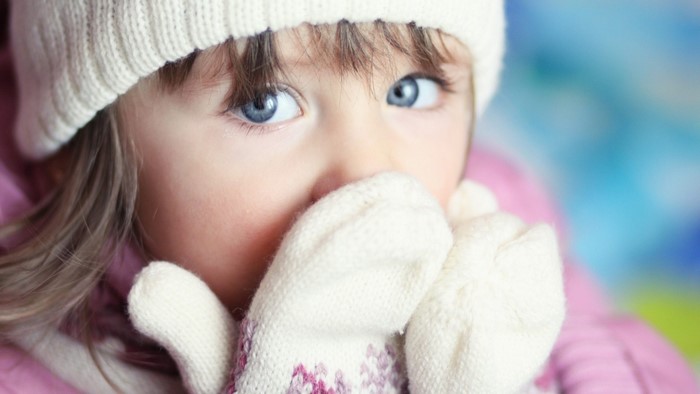 Close-up of a young girl with blue eyes wearing a winter hat and mittens