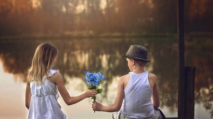 Boy gives flowers to girl by lake
