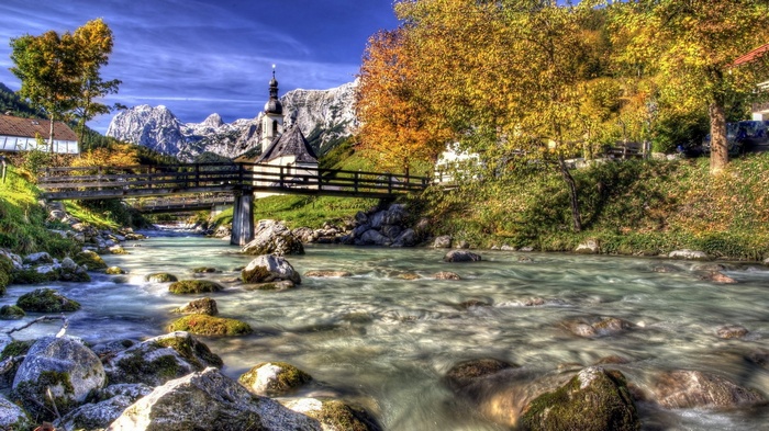 Wooden bridge over a river with a church and mountains