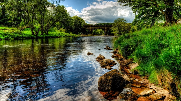 River flowing through a green landscape with a stone bridge