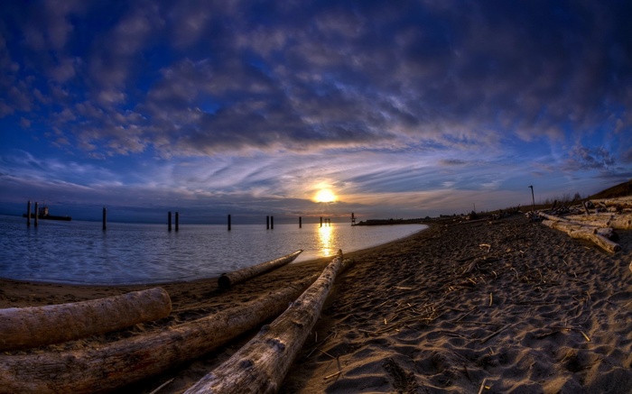 Sunset over a beach with driftwood and ocean pilings