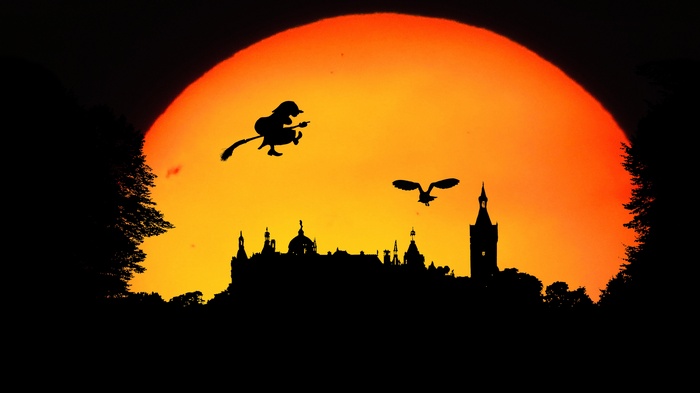 Witch flying on broomstick with owl over castle at sunset