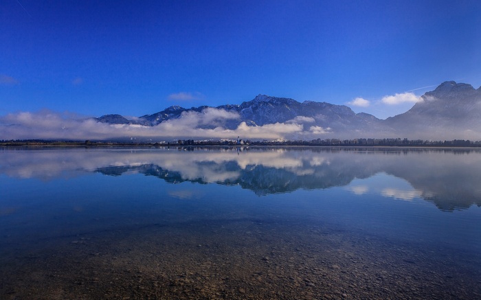 Lake reflecting mountains and clouds under a blue sky