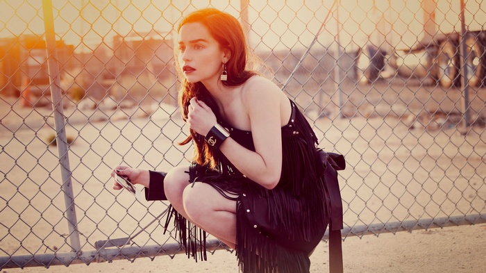 Emilia Clarke posing by a chain-link fence