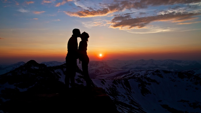 Couple kissing on mountain peak at sunset