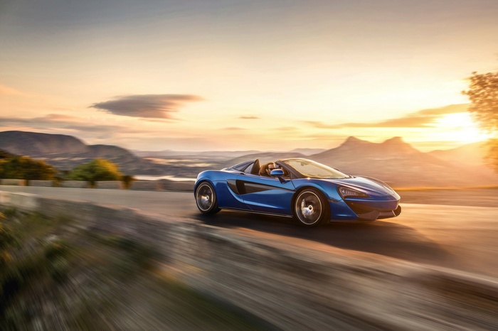 Blue McLaren 570S Spider driving at sunset